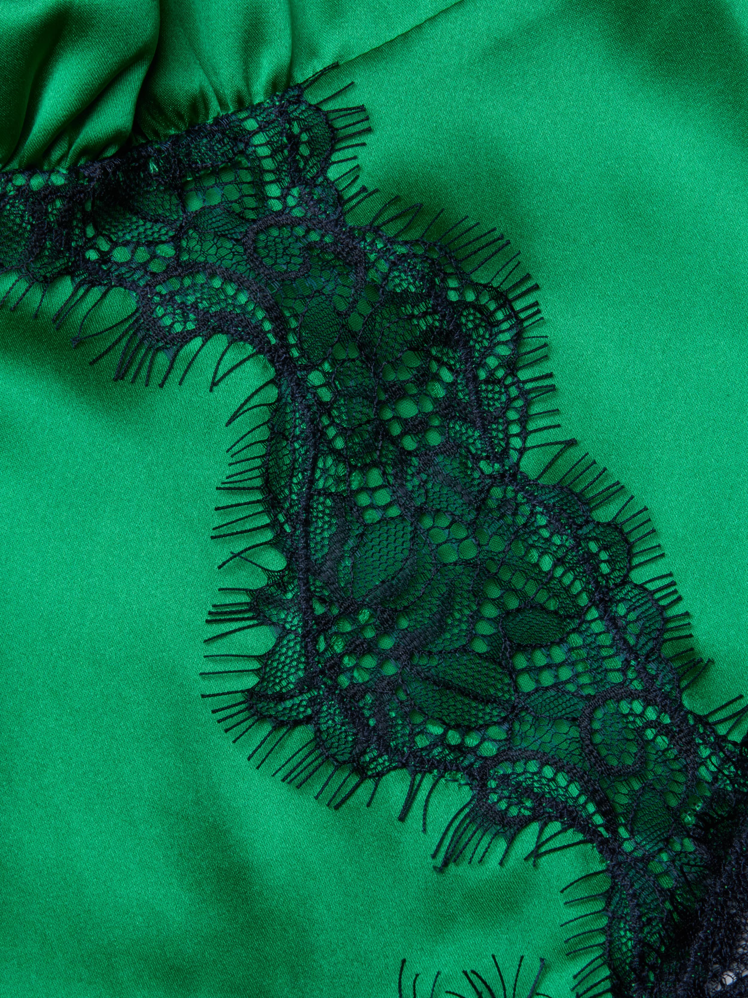 Close-up of the Kimber Silk Lace Camisole, showcasing green satin fabric with a black lace trim adorned with a floral pattern and delicate fringe.
