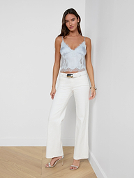 A woman wearing the Kimber Silk Lace Camisole in light blue, paired with white wide-leg pants and heels, stands against a plain white background.