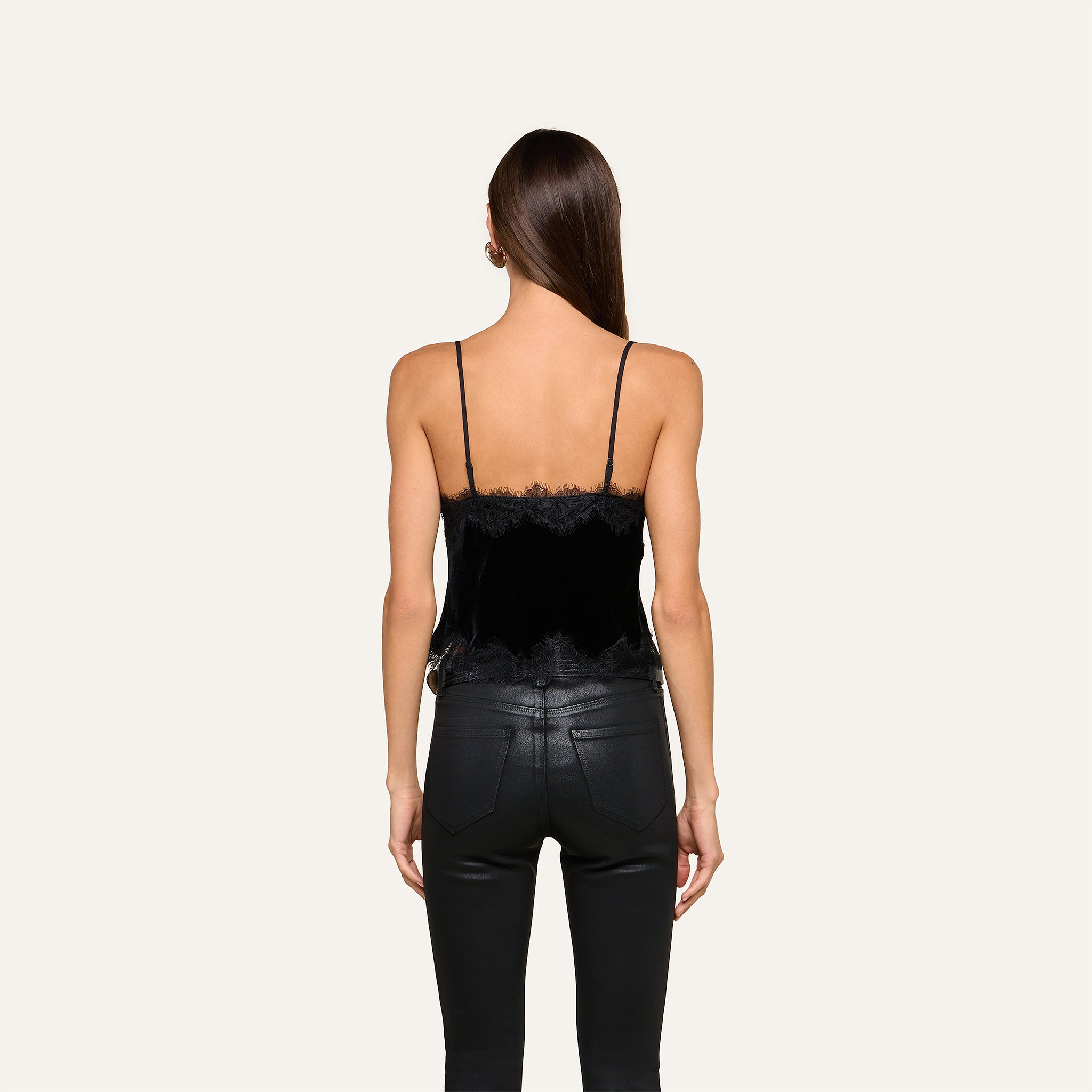 A woman with long brown hair stands facing away, wearing the Kimber Velvet Lace Camisole paired with black leather pants, set against a plain light background.
