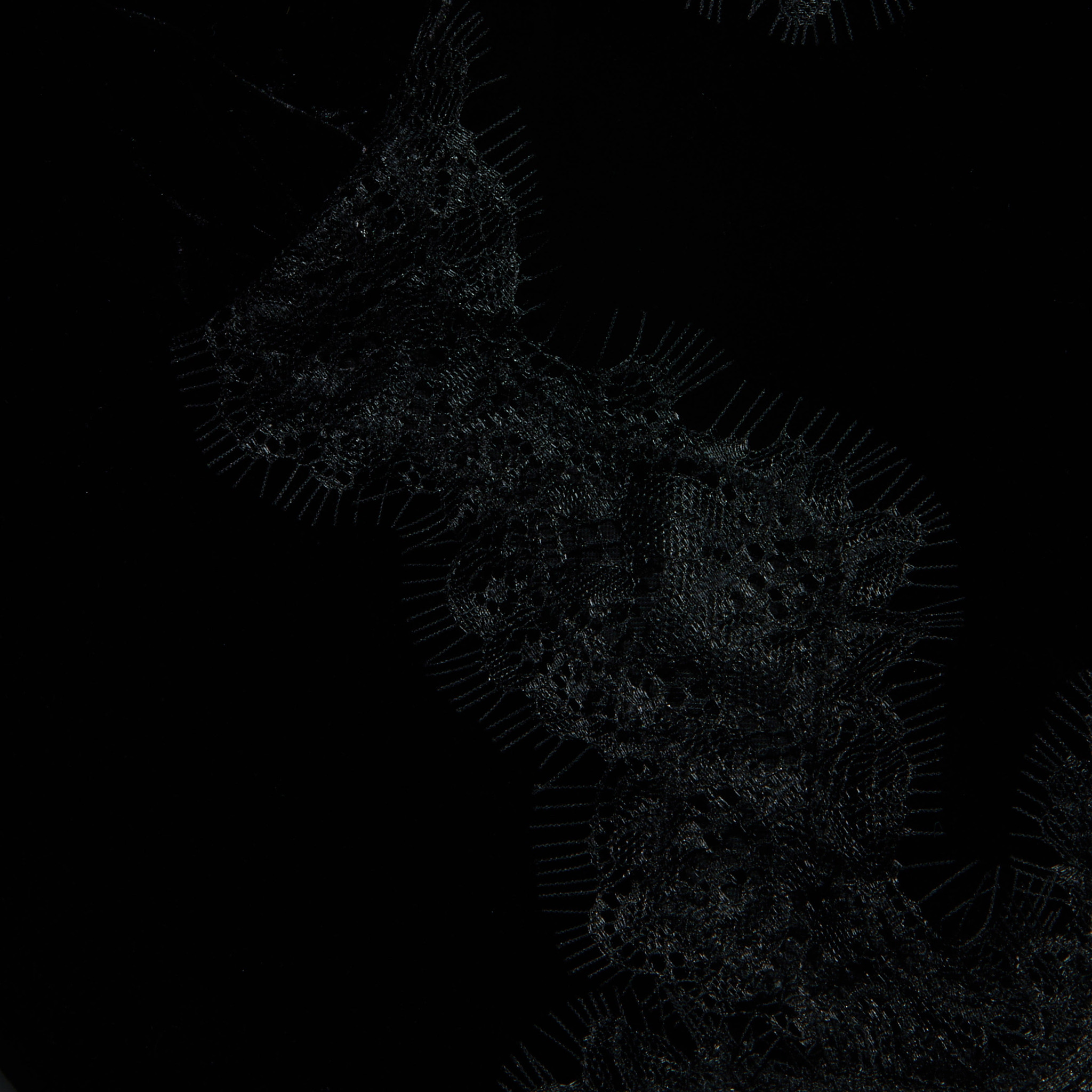 A dark, abstract pattern with faint, net-like textures and thin, radiating lines forms a winding, organic shape against a background reminiscent of the rich softness of black velvet—evoking the delicate elegance of the Kimber Velvet Lace Camisole.