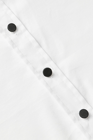 Close-up of the Blake Bodysuit reveals three evenly spaced black snap closures set diagonally against soft white organic cotton, with visible stitching along the closure strip.