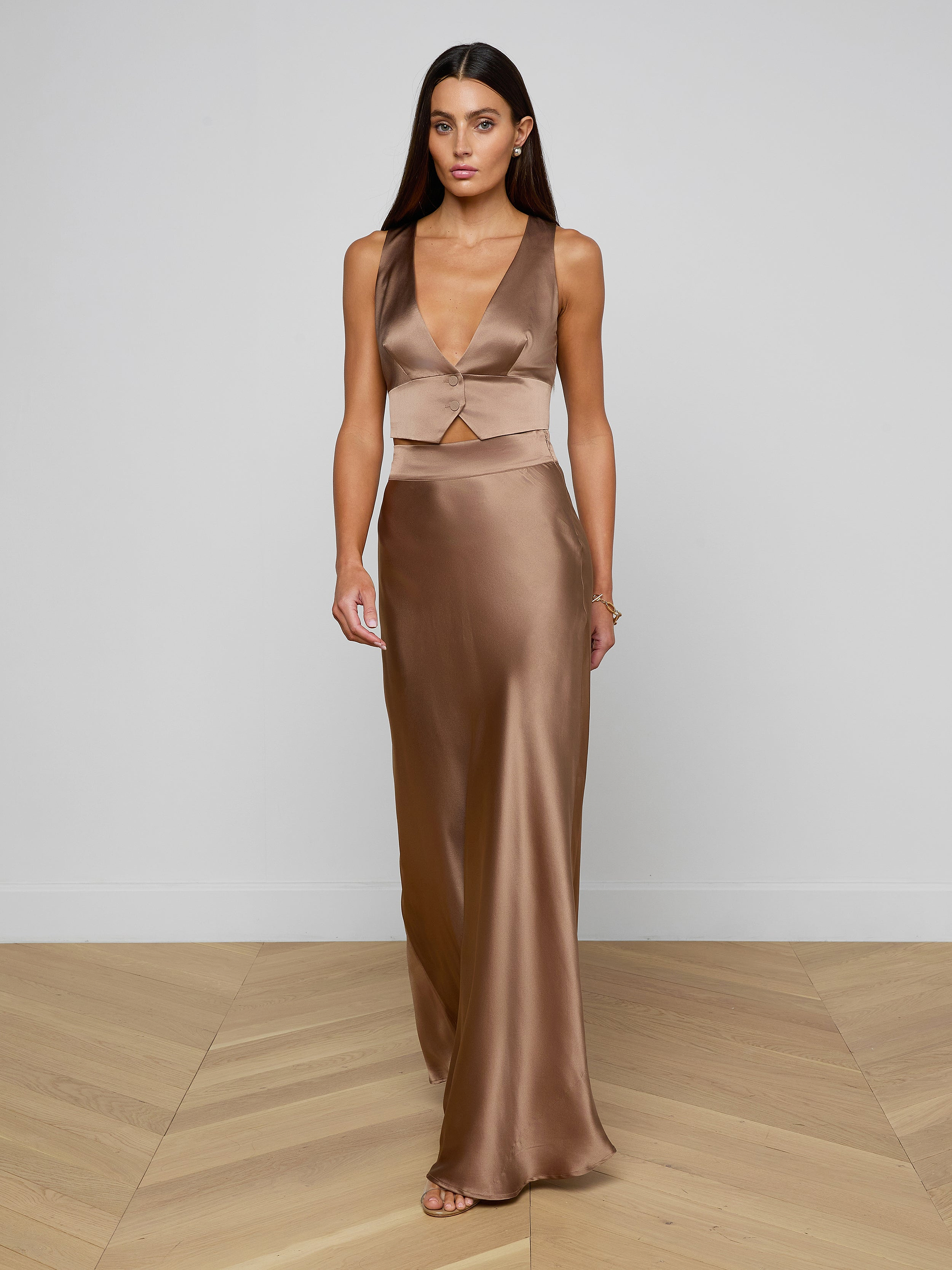 A woman in the Devony Silk Vest, a bronze satin tailored sleeveless crop top, paired with a long skirt, stands against a plain white background.
