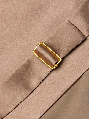 Close-up of the Devony Silk Vest's light brown fabric belt with a gold rectangular buckle, laid diagonally over matching silk. The soft, smooth material and delicate folds highlight the vest's refined elegance.
