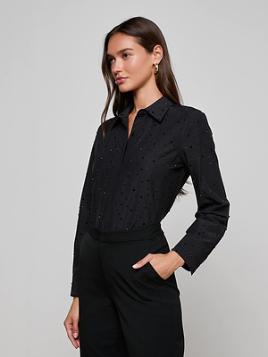 A woman with long brown hair stands against a plain light gray backdrop, wearing the L’AGENCE Ellery Crystal Shirt and black pants, with one hand in her pocket.