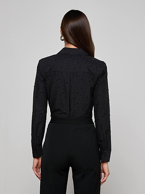 A woman with long brown hair, seen from behind, wears the L'AGENCE Ellery Crystal Shirt paired with high-waisted black pants against a plain light background.