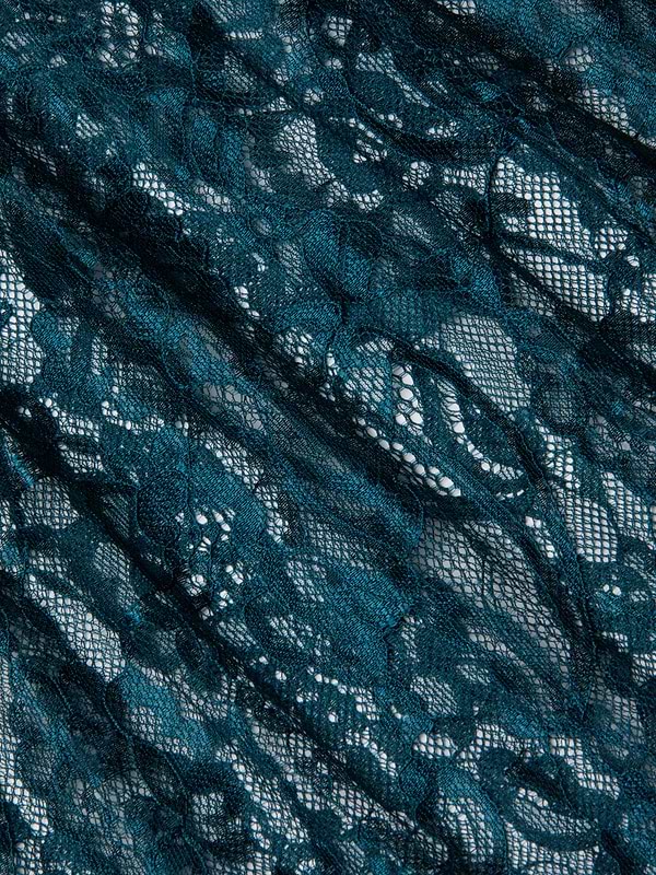 The Reece Lace Tie Neck Blouse features dark teal floral Chantilly lace with sheer sections and delicate, overlapping threads. Its slightly wrinkled texture adds depth, making it perfect for a stylish sheer lace blouse design.