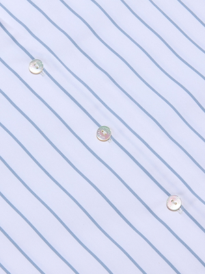 Close-up of the Deon Tie-Neck Blouse made from organic cotton-blend poplin featuring thin blue vertical stripes and three iridescent buttons sewn diagonally across the fabric.