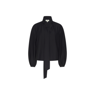 The Deon Tie-Neck Blouse is an oversized, black long-sleeve top made from organic cotton poplin. It features a high neckline with a dramatic long tie, blouson sleeves with buttoned cuffs, and a relaxed fit, shown against a plain white background.