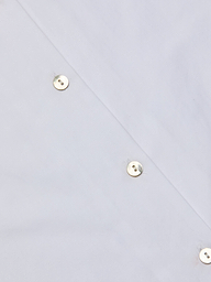 Close-up of the Deon Tie-Neck Blouse in white organic cotton poplin, featuring shiny metal snap buttons arranged diagonally, highlighting part of the garment. The reflective surface of the buttons adds a polished touch to the design.