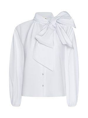 The Deon Tie-Neck Blouse is a white, oversized blouse made from organic cotton poplin, featuring a dramatic bow at the high collar, button-down front, blouson sleeves, and gently gathered cuffs.
