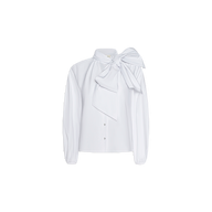 The Deon Tie-Neck Blouse is a white, long-sleeve oversized blouse crafted from organic cotton poplin, featuring a large, dramatic bow tied at the collar, elegant blouson sleeves, and a button-down front. It is displayed on a plain white background.