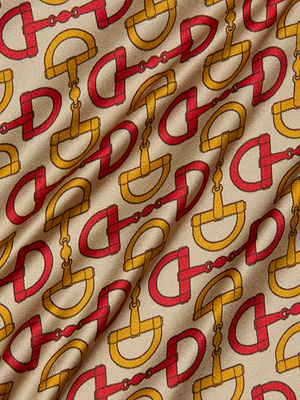 A close-up of the Calista Silk Camisole by L’AGENCE shows beige silk with interlocking gold and red horse bit print, resembling equestrian tack. The slightly wrinkled fabric is ideal for a chic cropped top or camisole.
