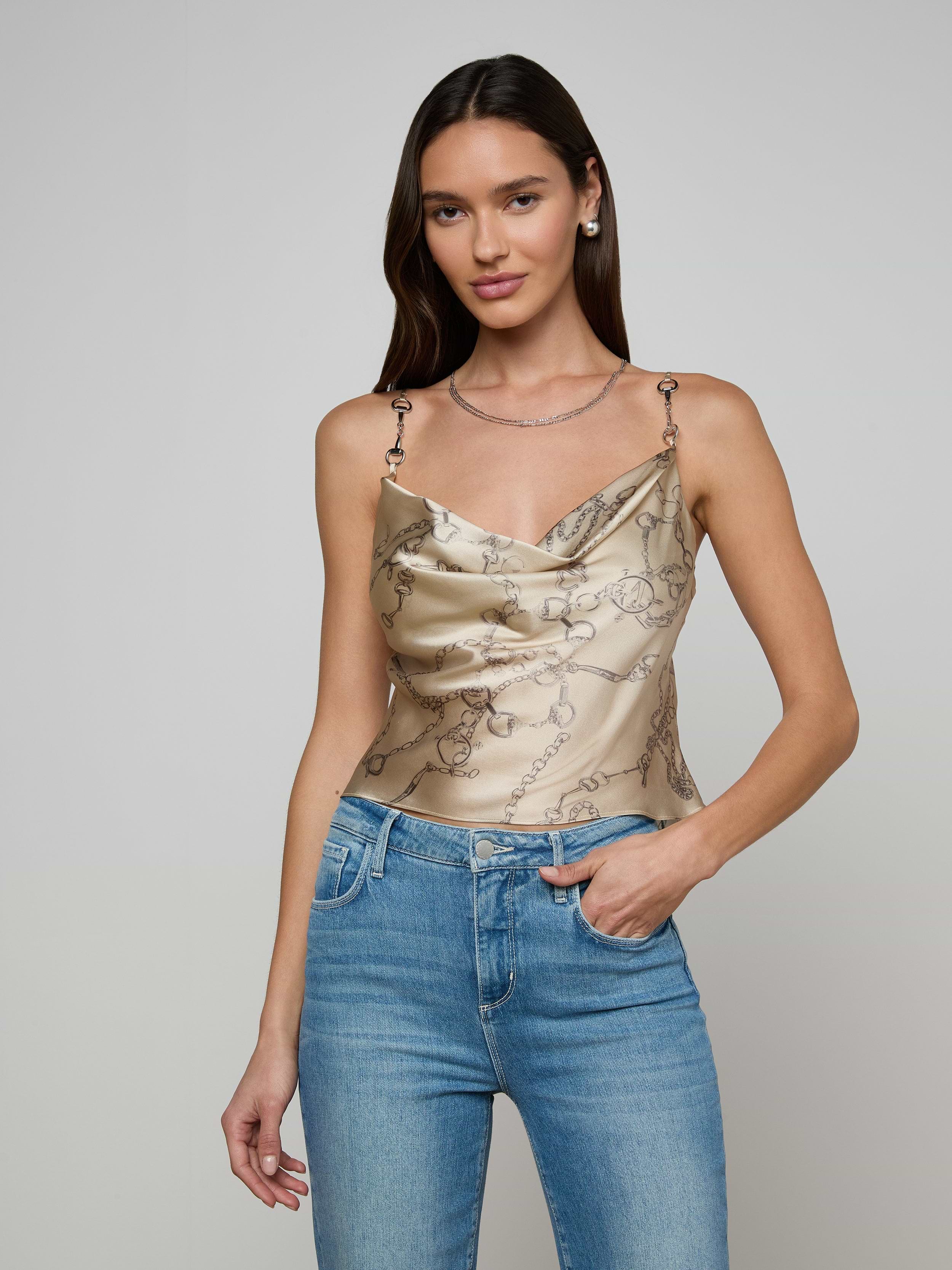 A woman with long dark hair wears the Calista Silk Camisole, a cropped top featuring a horse bit chain print, paired with blue jeans and standing against a plain light background.