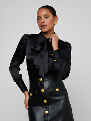 A woman wearing the Honey Silk Blouse styled with a black leather skirt featuring large gold buttons, posing confidently against a plain light gray background.
