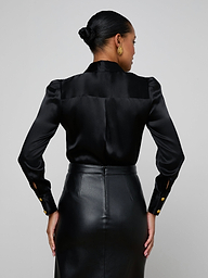 A woman is shown from the back wearing the Honey Silk Blouse, styled with a high-waisted black leather skirt, standing against a plain light background.