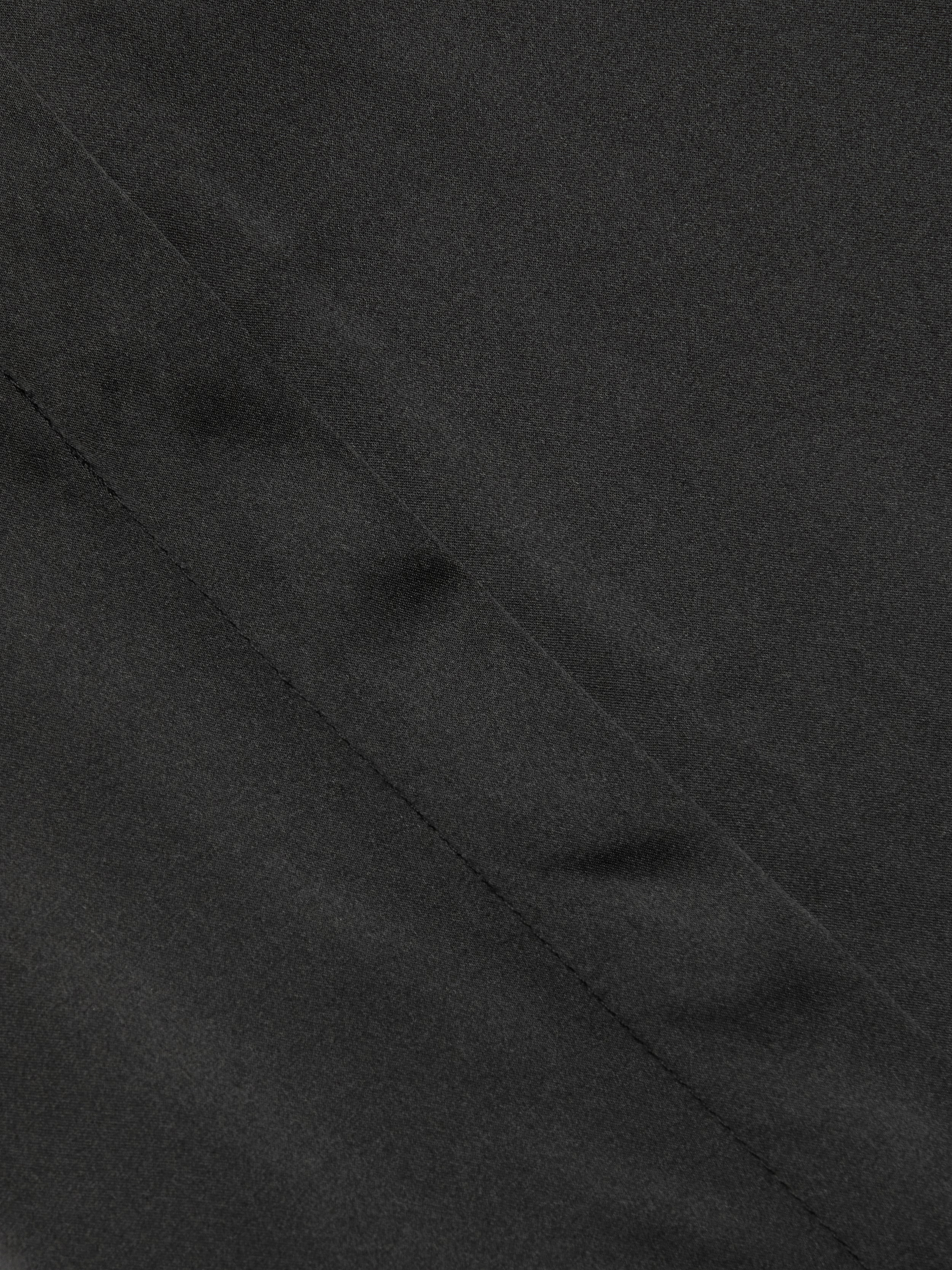 Close-up of the Honey Silk Blouse in black, showcasing a diagonal seam and subtle textured finish.