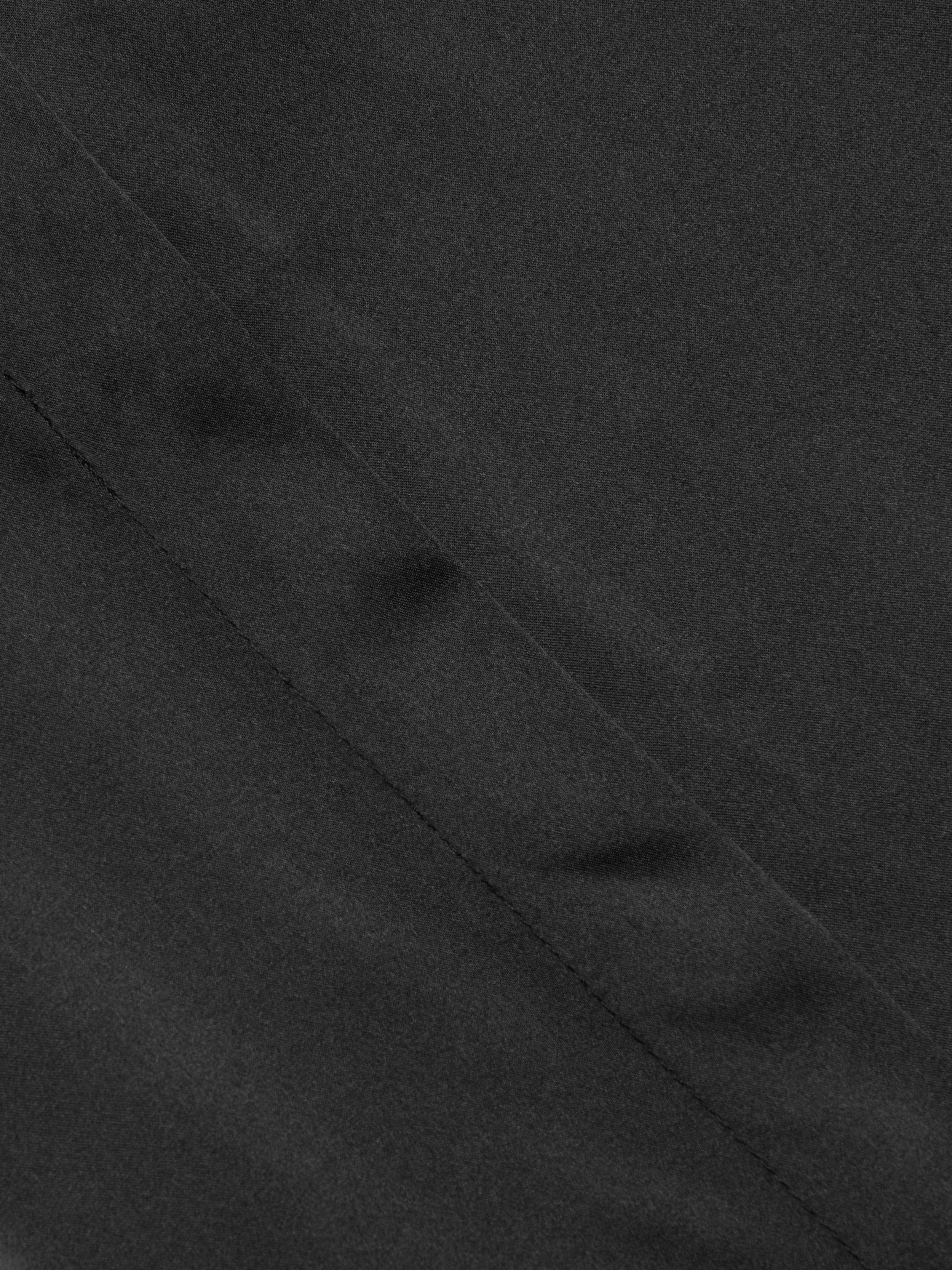 Close-up of the Honey Silk Blouse in black, showcasing a diagonal seam and subtle textured finish.