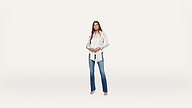 A woman stands facing forward, wearing a white blouse with puffed sleeves, blue jeans, and open-toed shoes against a plain white background.