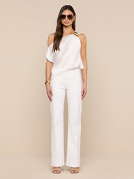 A woman poses against a beige background wearing the Driselle Scarf Top—white satin with a gold buckle—styled with wide-leg pants, sunglasses, gold jewelry, and heeled sandals.