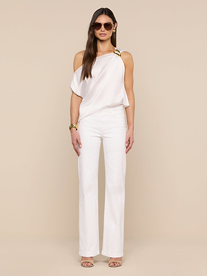 A woman poses against a beige background wearing the Driselle Scarf Top—white satin with a gold buckle—styled with wide-leg pants, sunglasses, gold jewelry, and heeled sandals.