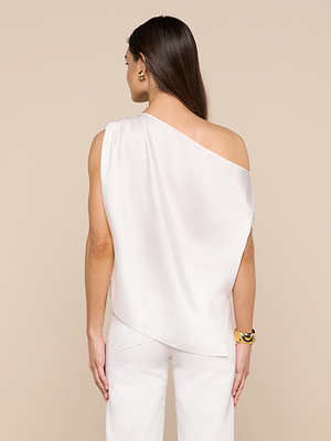 A woman with long brown hair stands facing away, wearing the Driselle Scarf Top in white satin and matching pants, accessorized with gold earrings and a bracelet against a beige background.