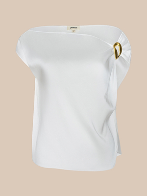 The Driselle Scarf Top is a white satin off-shoulder blouse with a loose, draped fit and a gold buckle accent on one side, shown against a beige background.