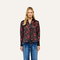 A woman wearing a black Sona Silk Blouse with a red cherry print and blue jeans.