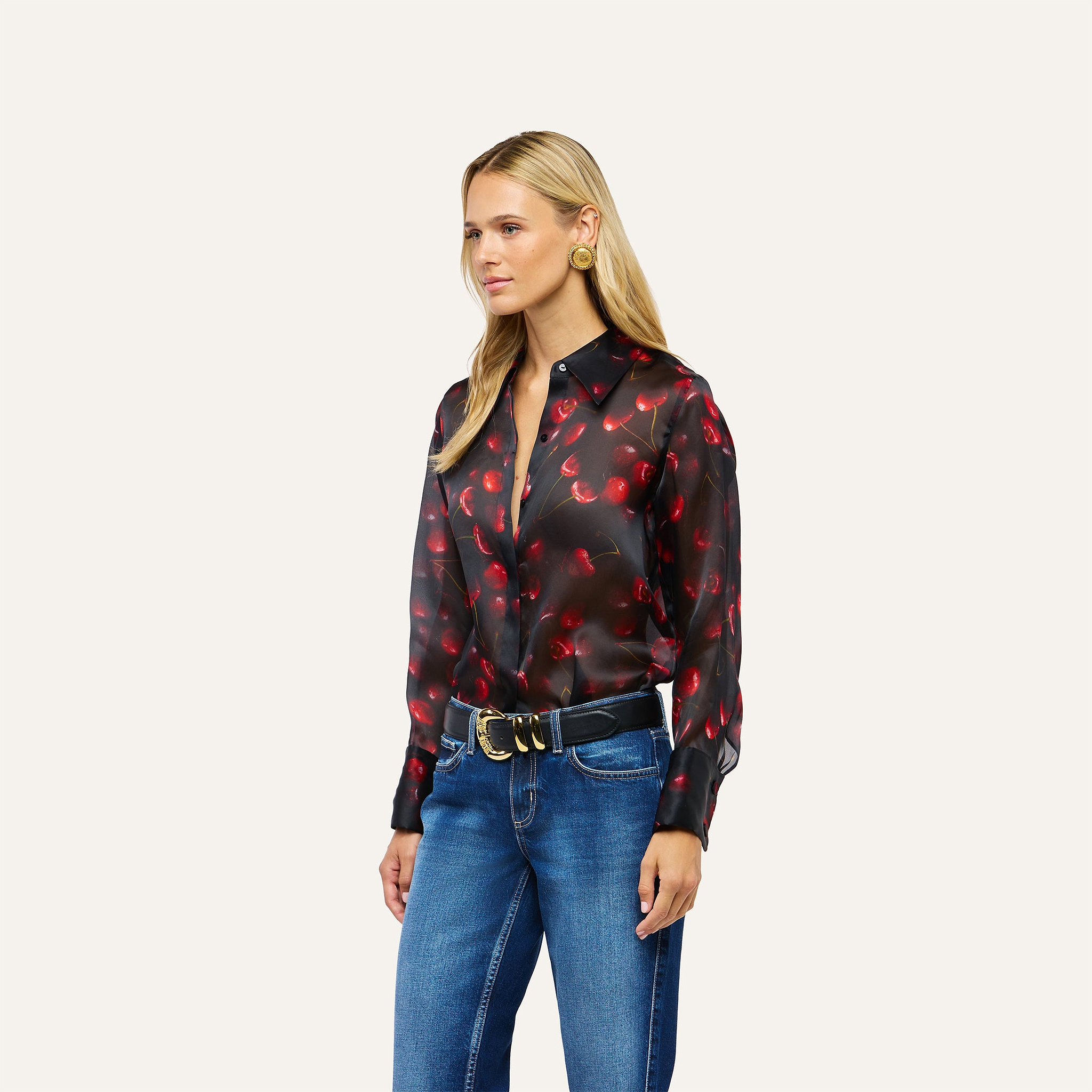 A person wearing a black long-sleeved button-down Sona Silk Blouse with a cherry pattern and blue jeans.