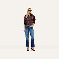 A person wearing a long-sleeved black Sona Silk Blouse with red floral accents, blue ripped jeans, and black high heels.