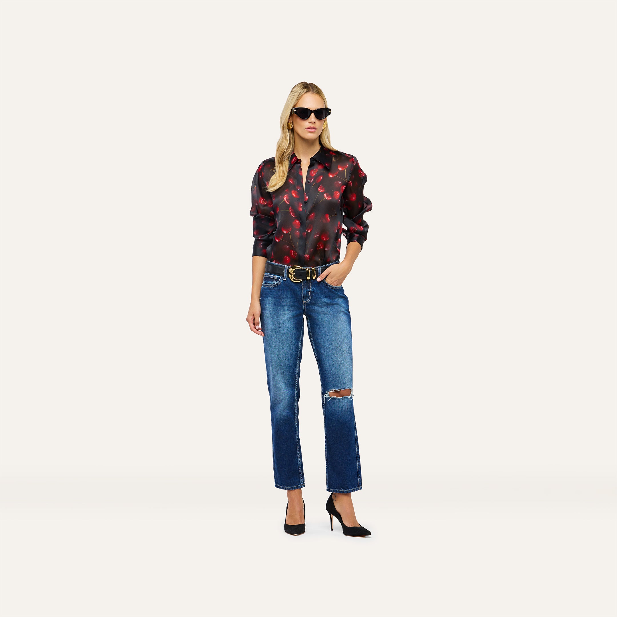 A person wearing a long-sleeved black Sona Silk Blouse with red floral accents, blue ripped jeans, and black high heels.