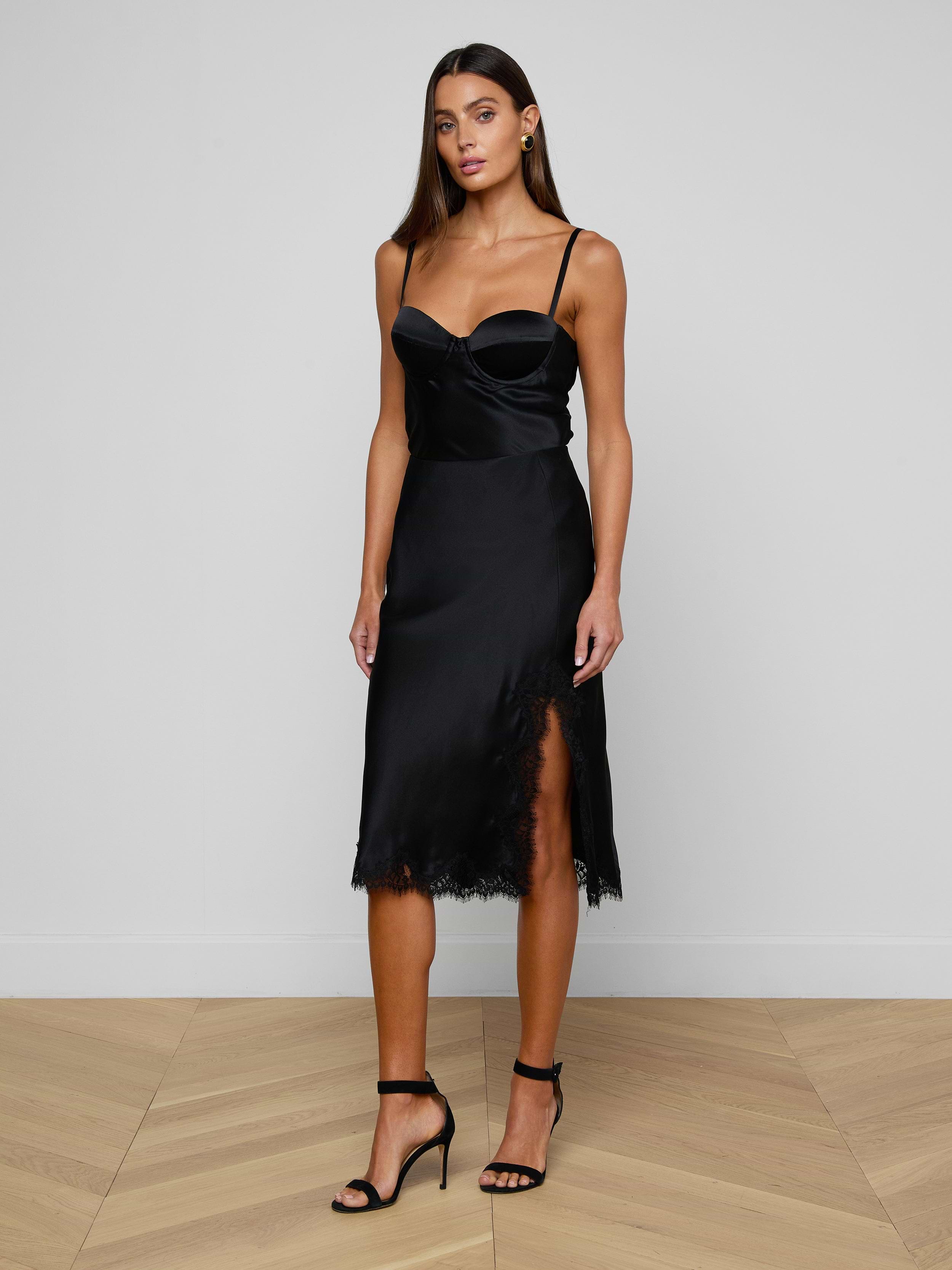 Wearing the Orlina Silk Camisole, a woman stands against a plain white background. The camisole features underwire cups, spaghetti straps, and a thigh-high slit, and she completes the look with black high-heeled sandals.