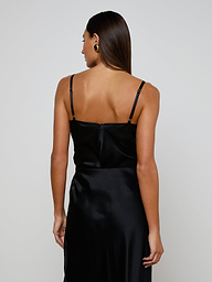A woman with straight brown hair is seen from behind, standing against a plain light background, wearing the Orlina Silk Camisole in black with thin straps.
