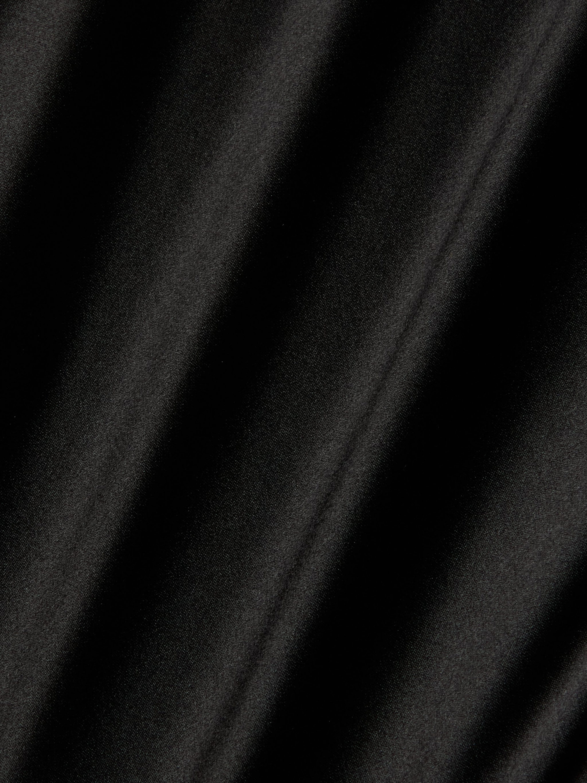 A close-up of the Orlina Silk Camisole in black, highlighting its luxurious silk fabric with soft diagonal shadows and folds that form a pattern of alternating light and dark areas.