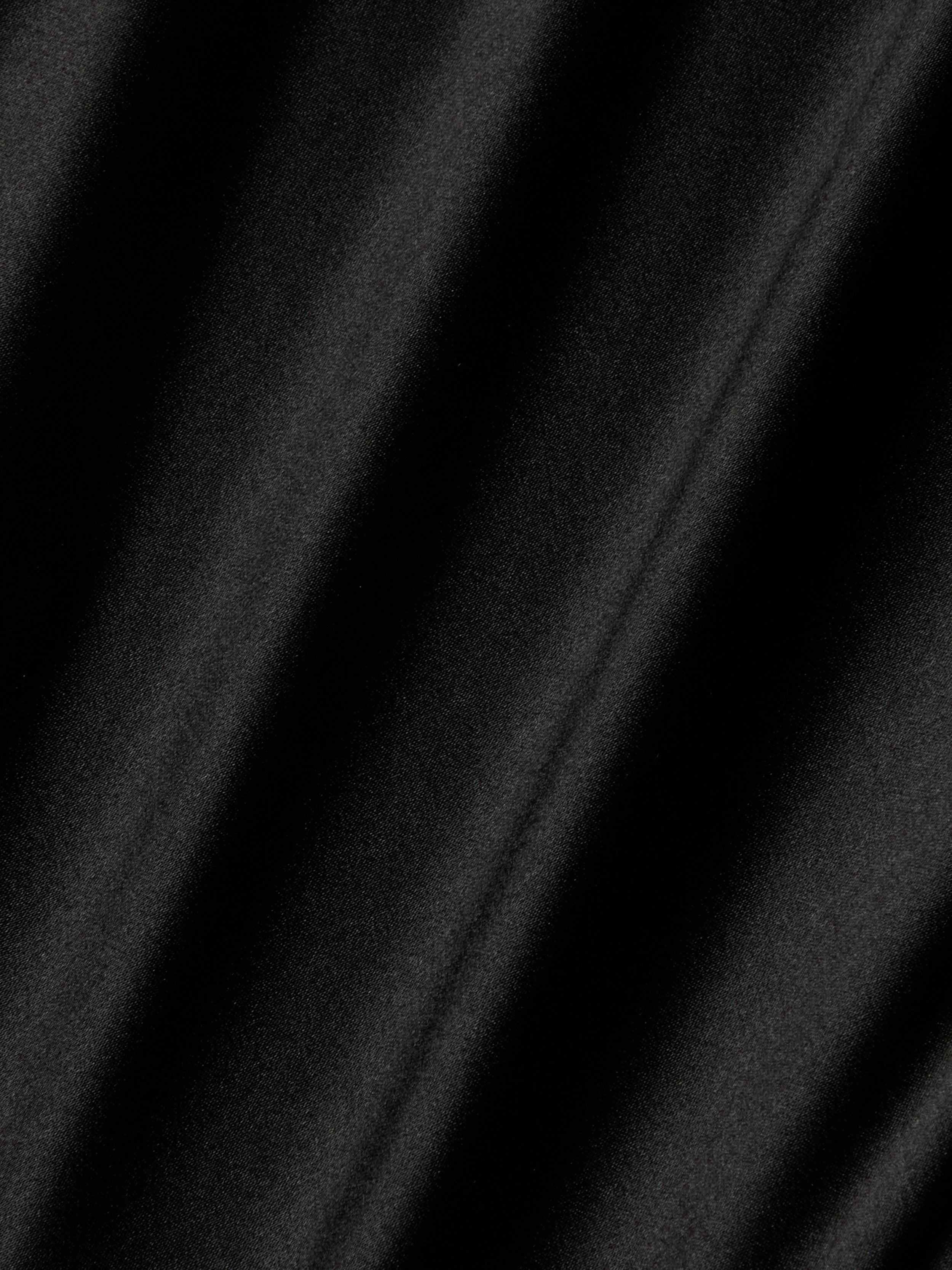 A close-up of the Orlina Silk Camisole in black, highlighting its luxurious silk fabric with soft diagonal shadows and folds that form a pattern of alternating light and dark areas.