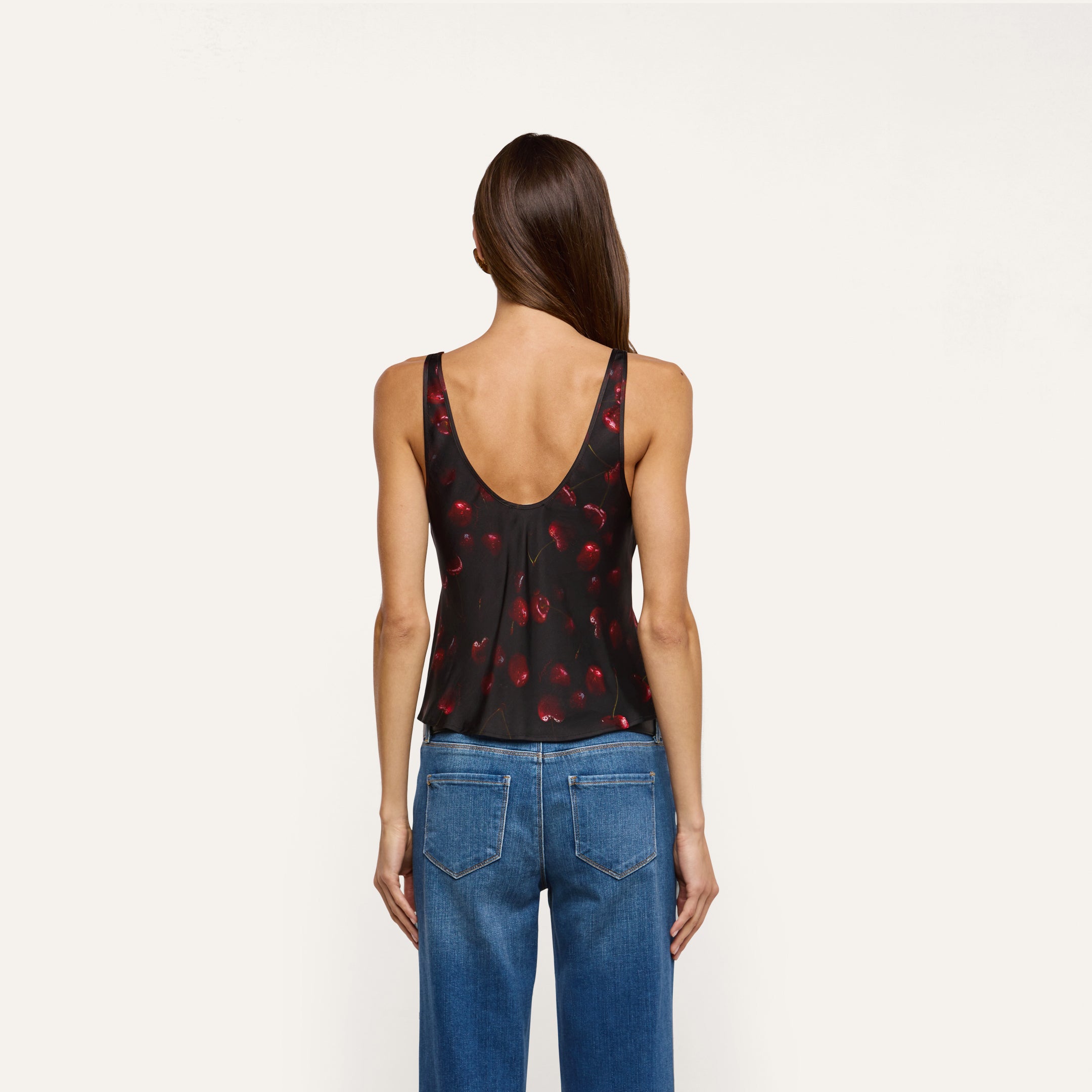 Back view of a person wearing a black cherry print Eddie Satin Tank with a scoop neckline and blue jeans.