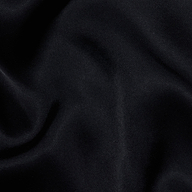 The Eddie Tank features soft, black fabric with a smooth texture and gentle, flowing folds that create subtle highlights and shadows across the material, enhanced by its flattering drape.
