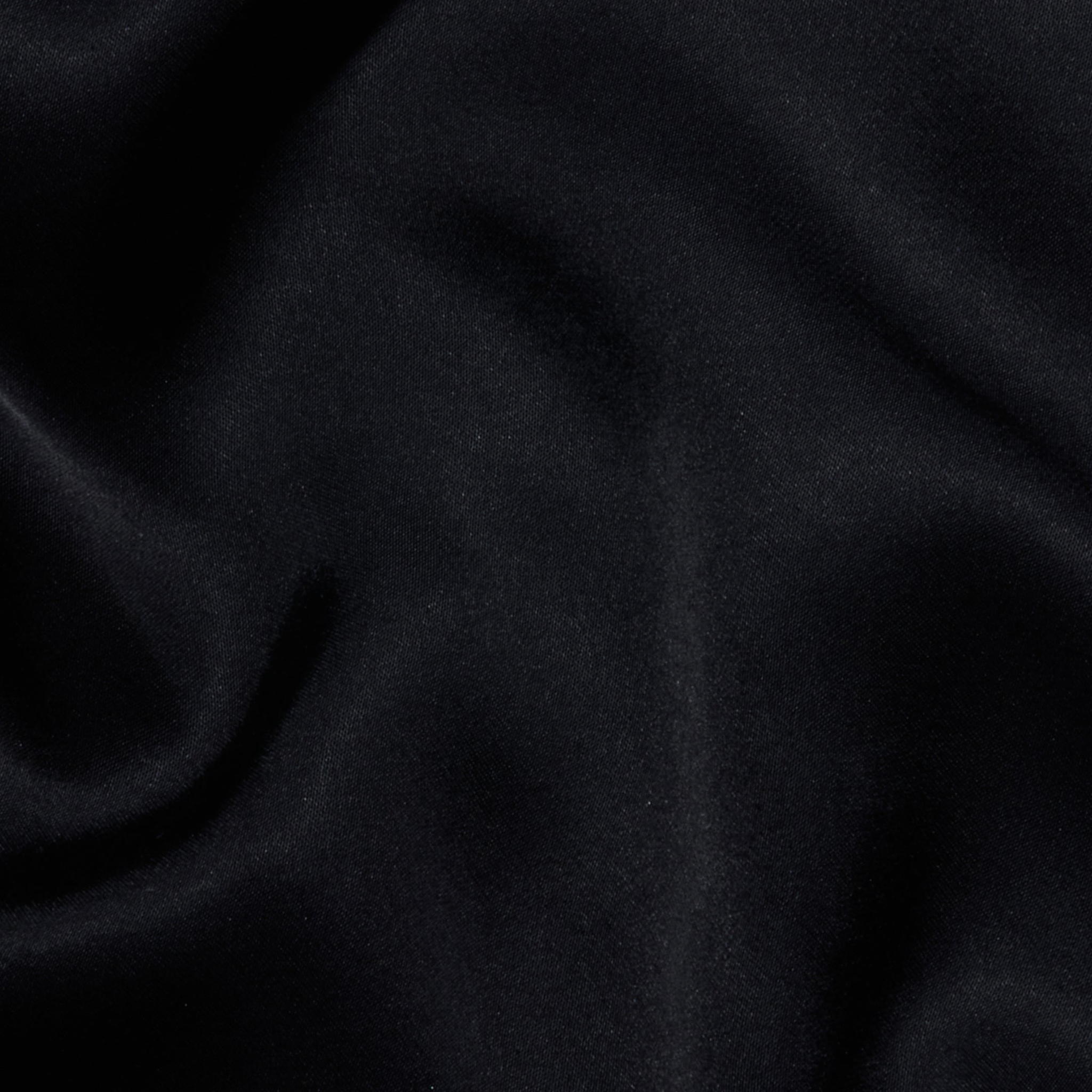 The Eddie Tank features soft, black fabric with a smooth texture and gentle, flowing folds that create subtle highlights and shadows across the material, enhanced by its flattering drape.