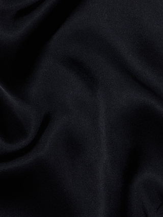 The Eddie Tank features a black velvet fabric with soft folds and a smooth, subtly lustrous texture that captures the luxurious essence of bias-cut satin. Its plush material displays decadent highlights and shadows, accentuating the depth and richness of the tank’s surface.