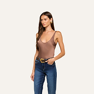 A woman wearing the Eddie Tank in cardamom brown—a bias-cut satin tank top with a scoop neckline—paired with blue jeans and a belt, poses with one hand in her pocket against a plain light background.