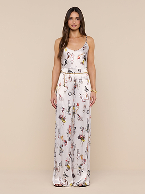 A woman faces forward against a plain beige background, wearing the Charmy Satin Camisole jumpsuit with a vibrant butterfly print and wide-leg pants.