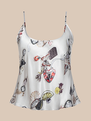 The Charmy Satin Camisole is a white satin top with thin straps, decorated with a butterfly print, watches, chocolates, seashells, and heart motifs—all set against a beige background.