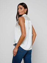 A woman with long dark hair, wearing the Phoebe Silk Blouse and blue jeans, stands looking over her shoulder against a plain light background.