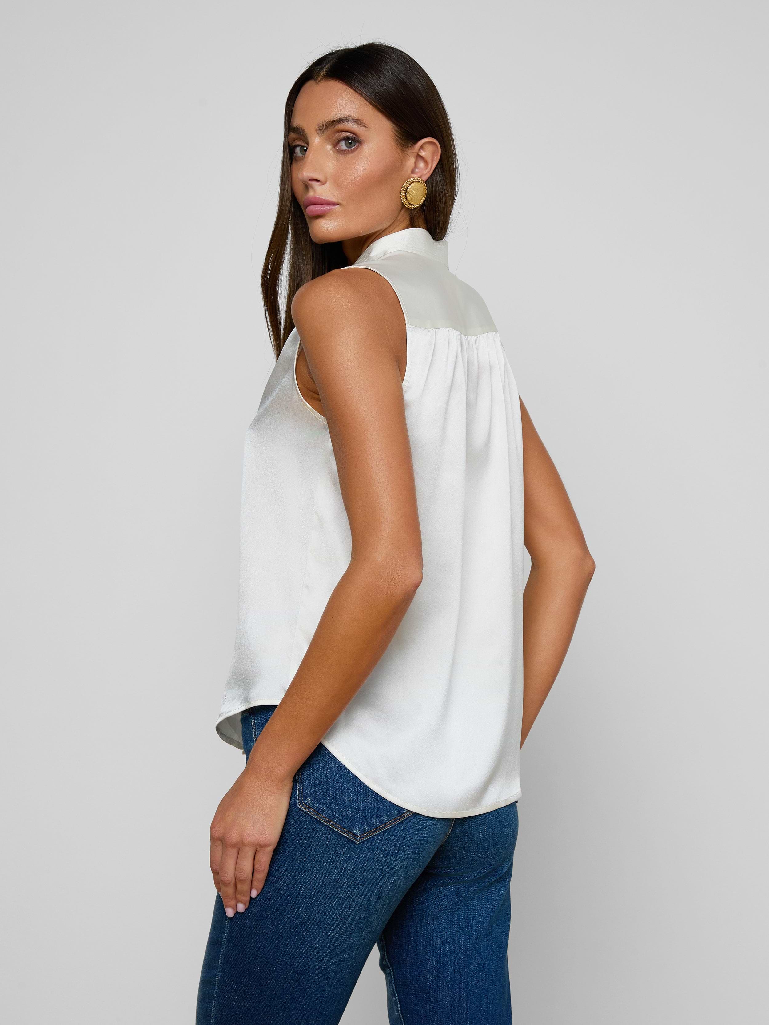 A woman with long dark hair, wearing the Phoebe Silk Blouse and blue jeans, stands looking over her shoulder against a plain light background.
