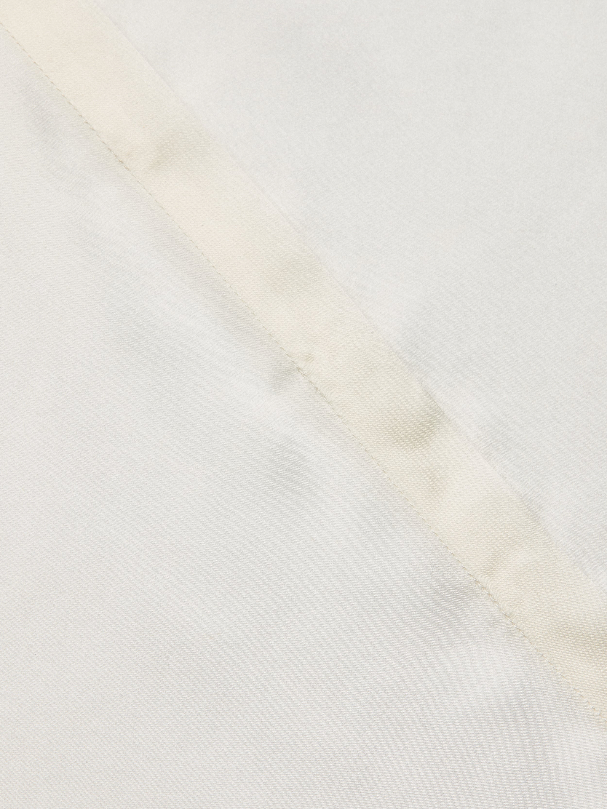 Close-up of the Phoebe Silk Blouse in a light-colored silk charmeuse, featuring a diagonal seam that highlights its smooth texture and subtle stitching detail.
