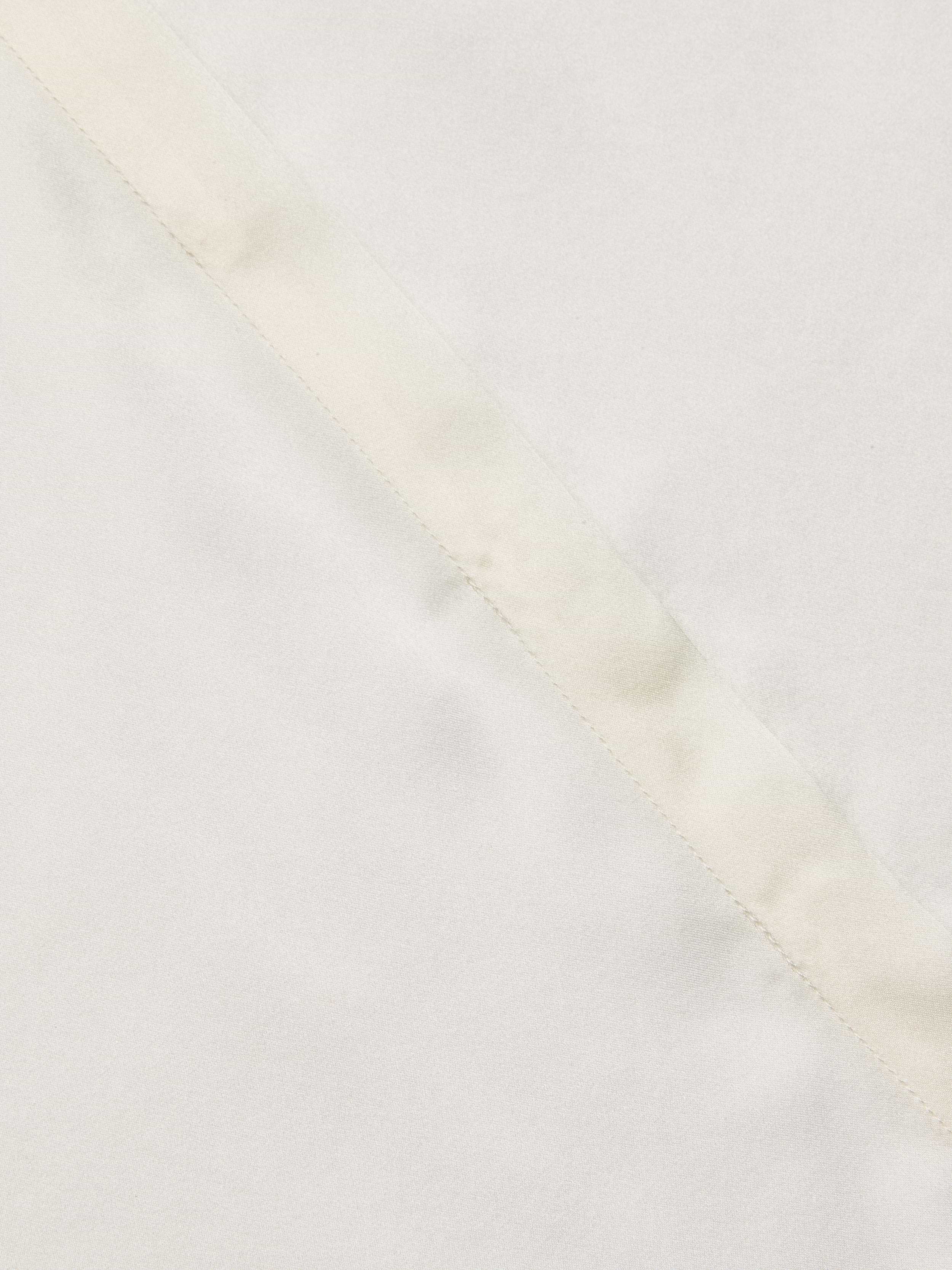 Close-up of the Phoebe Silk Blouse in a light-colored silk charmeuse, featuring a diagonal seam that highlights its smooth texture and subtle stitching detail.