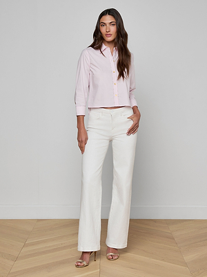 A woman stands indoors on a wooden floor, wearing the Fawn Shirt paired with high-waisted white wide-leg pants and beige high-heeled sandals, posing with one hand in her pocket.