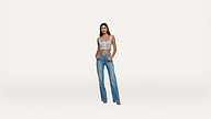 A woman stands against a plain white background, wearing a patterned crop top, high-waisted blue jeans, and heeled sandals, with one hand in her pocket and a neutral expression.