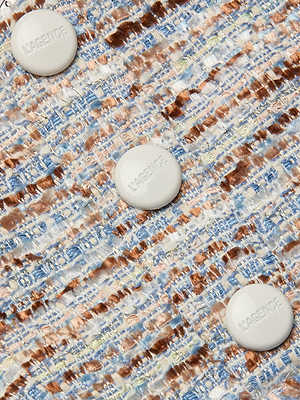 Close-up of the Muno Tweed Top’s textured fabric in blue, brown, and white, finished with three large round white LAGENCE-embossed buttons and subtle frayed edges for added detail.