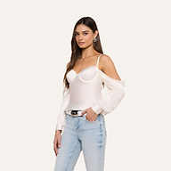 A woman wearing the Saya Satin Top—a white off-the-shoulder satin top with spaghetti straps—paired with light blue jeans stands against a plain background, looking at the camera with a relaxed expression.