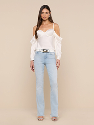 A woman stands against a plain white background wearing the Saya Satin Top in white, light blue jeans, a black belt, and open-toe heels. Her arms are relaxed by her sides and her long, straight hair is loose.